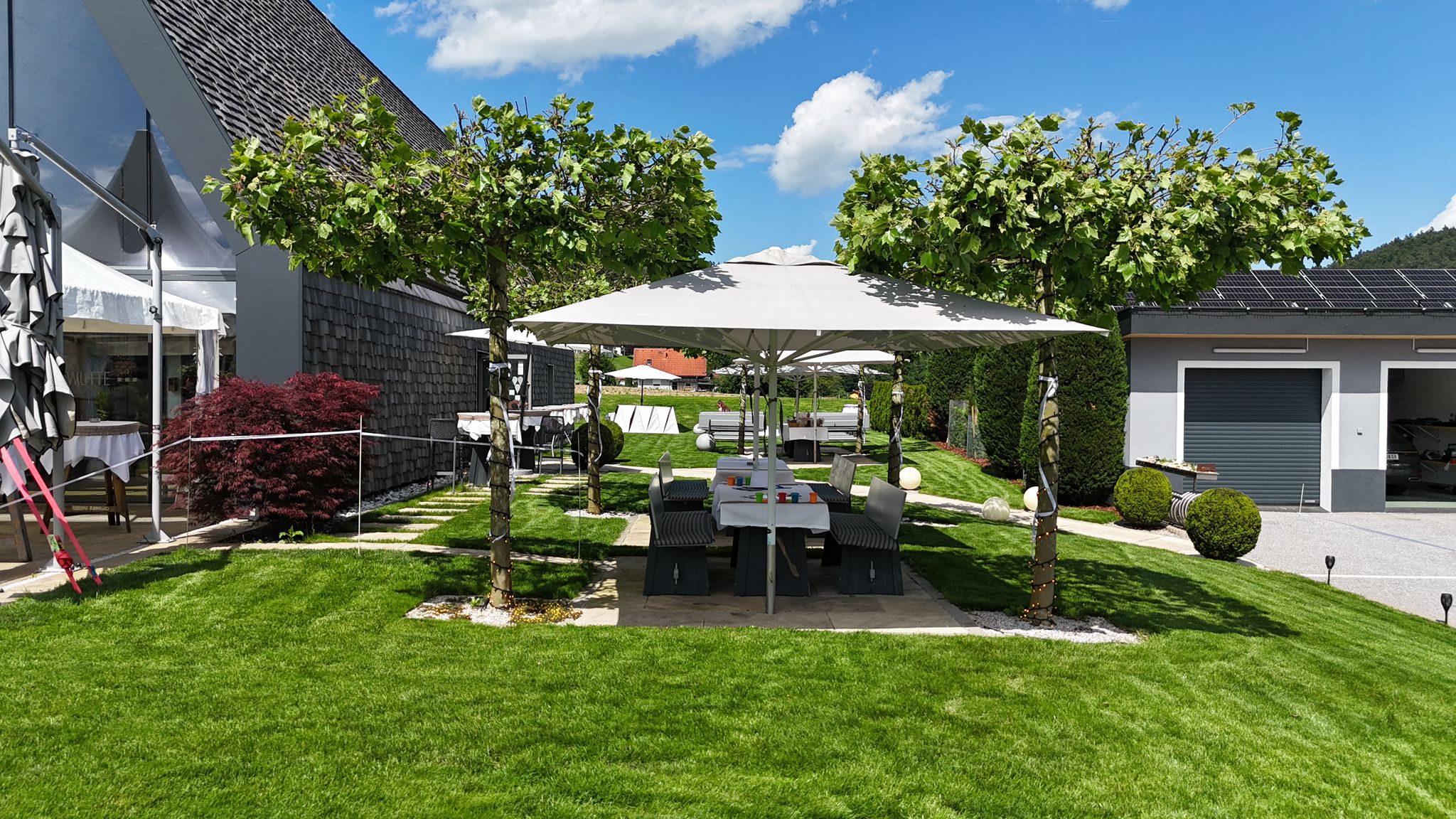 Langer, festlich gedeckter Tisch im Garten unter weißen Sonnenschirmen.