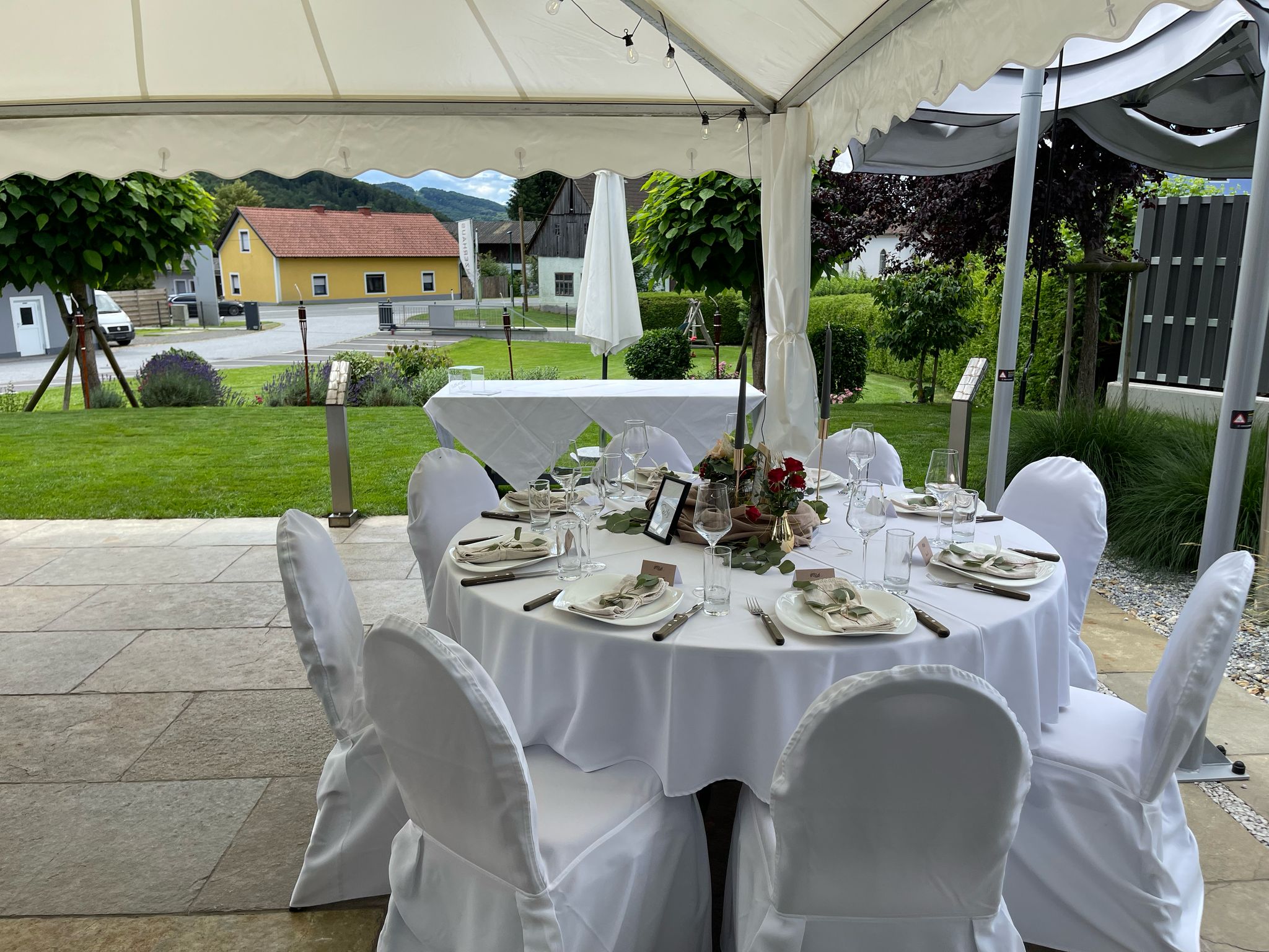 Rund gedeckter Tisch im Zelt mit weißer Husse und Blick in den Garten.