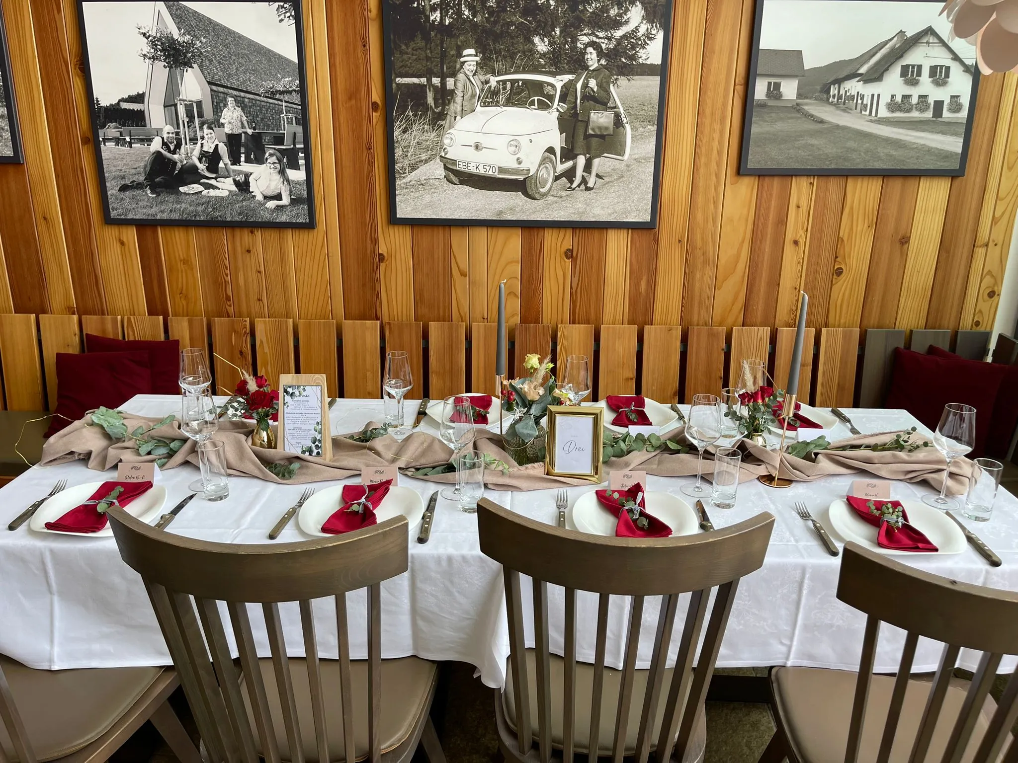 Festlich gedeckter langer Tisch im Innenraum mit roter Serviettendeko und historischen Fotos an der Wand.